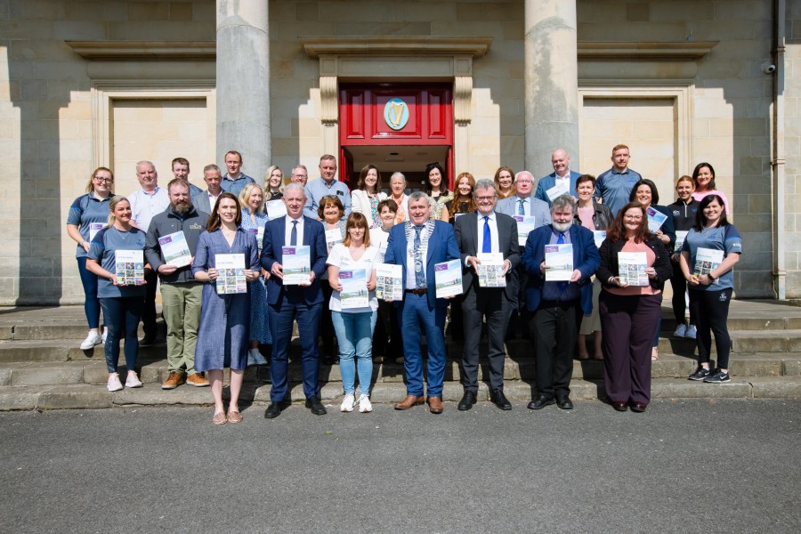 A group of 30 people lined up smiling outside Cavan Courthouse holding the two new Cavan Sports Partnership strategies. Cathaoirleach Cllr TP O'Reilly is at the front wearing the chain of office